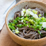 Soba noodles in bowl with scallions and toasted white sesame seeds.