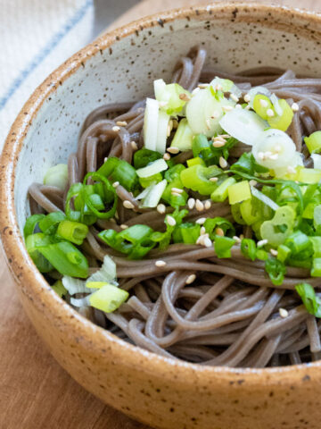 Soba noodles in bowl with scallions and toasted white sesame seeds.