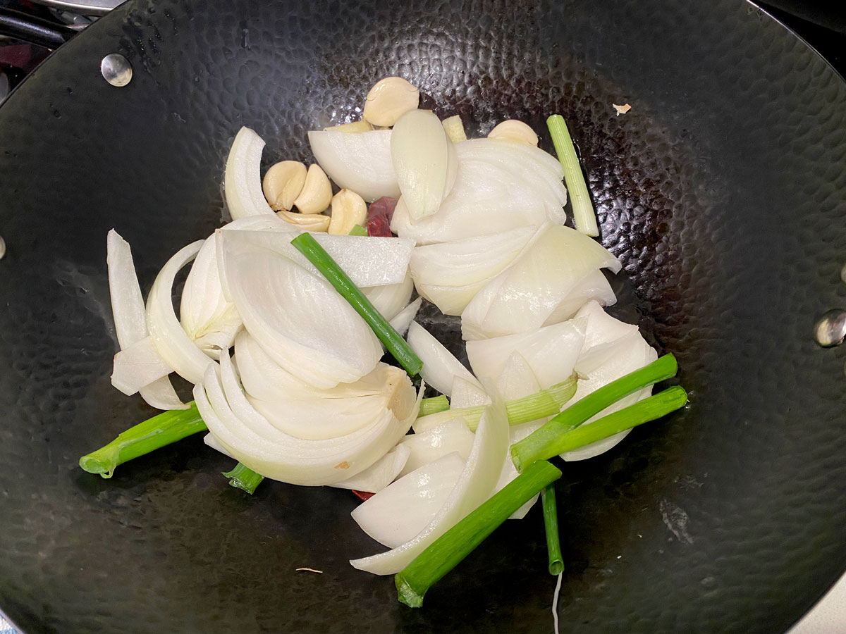 Onion, garlic, red chili and scallion in wok.