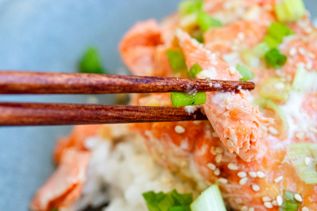 Piece of baked salmon picked up by wooden chopsticks.