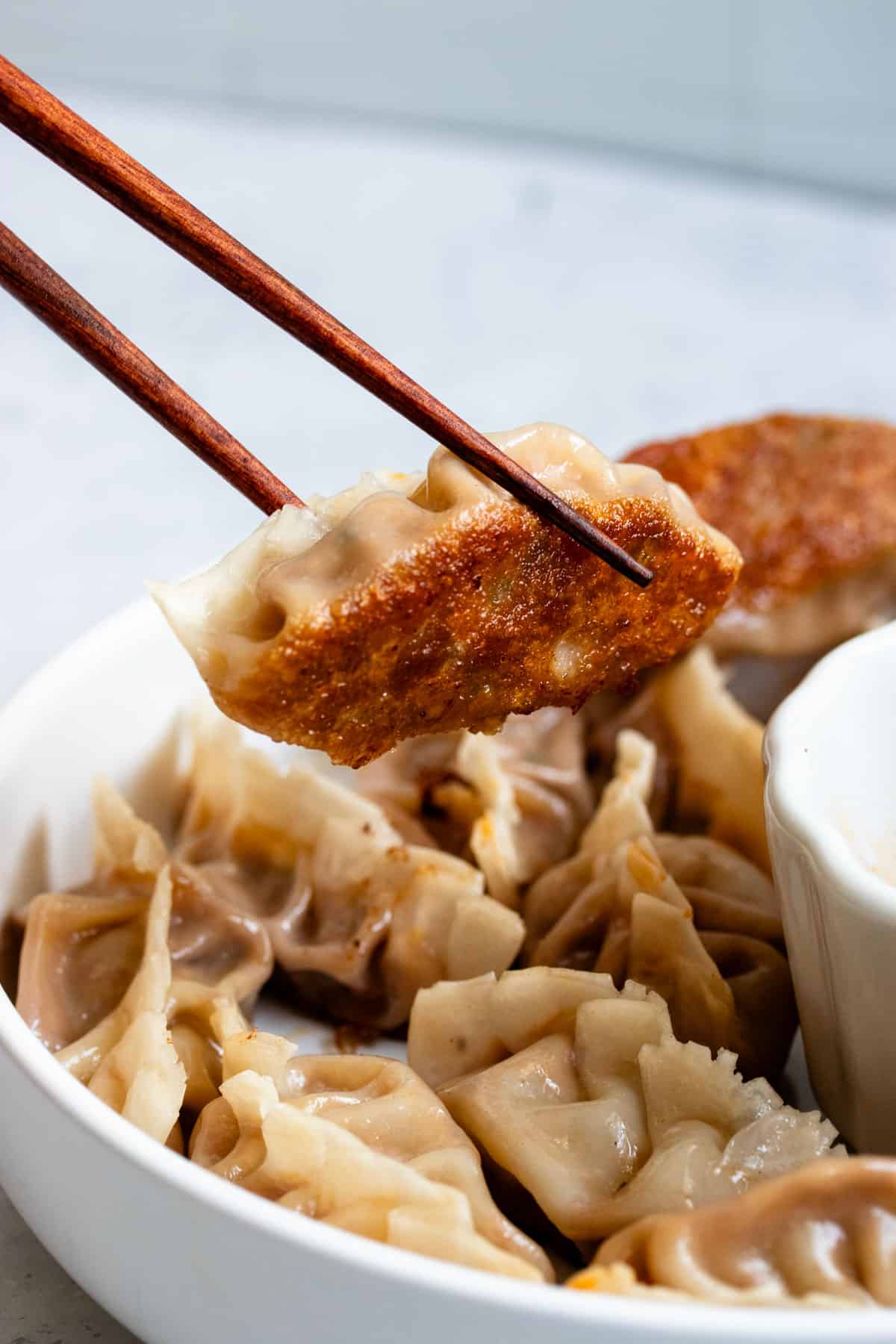 Crispy pork dumplings held up by wooden chopsticks.